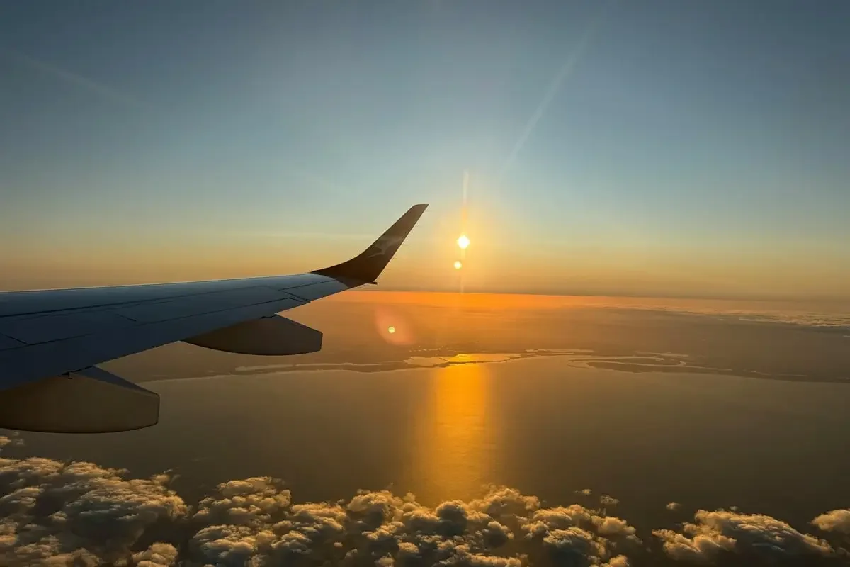 View of airplane wing through window during sunrise, representing the start of a mystery trip adventure
